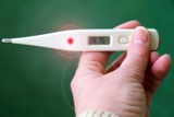 Eine Hand hält ein Fieberthermometer. Symbolbild für Fieber.