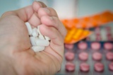 Eine Hand hält mehrere Tabletten, im Hintergrund sieht man unscharf weitere Tabletten.