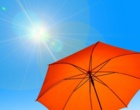 Ein aufgespannter Sonnenschirm unter strahlender Sonne und blauem Himmel.