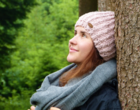 Eine Frau lehnt sich entspannt im Wald an einen Baumstamm.