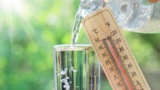 Wasserglas, Wasserflasche und Thermometer mit 39 Grad Celsius vor sonnigem Hintergrund.