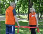 Ein Mann und eine Frau stehen sich in einem Park gegenüber und halten ein Gymnastikband zwischen sich.