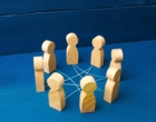 Im Kreis aufgestellte Holzfiguren sind mit einem Fadem miteinander verbunden. Symbolbild für Vernetzung.