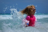 Ein Mädchen mit Sonnenschutzkleidung und Sonnenbrille springt im Meer umher.