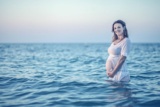 Eine schwangere Frau steht im Meer.