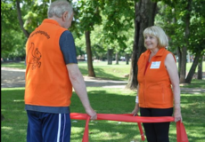 Ein Mann und eine Frau stehen sich in einem Park gegenüber und halten ein Gymnastikband zwischen sich.