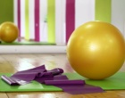 Auf dem Boden einer Sporthalle liegen ein Gymnastikball, eine Matte und ein Fitnessband.