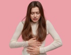 Eine junge Frau hält sich mit beiden Händen den Bauch. Symbolbild für Bauchschmerzen.