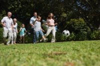 Eine Mehr-Generationenfamilie rennt über eine Wiese und spielt Fußball.