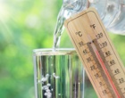 Wasserglas, Wasserflasche und Thermometer mit 39 Grad Celsius vor sonnigem Hintergrund.