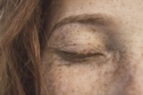 Ausschnitt eines Gesichts einer rothaarigen Frau mit Sommersprossen.