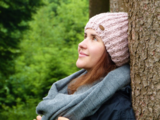 Eine Frau lehnt sich entspannt im Wald an einen Baumstamm.