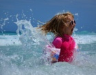 Ein Mädchen mit Sonnenschutzkleidung und Sonnenbrille springt im Meer umher.