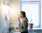 Eine Frau steht im Badezimmer vor einem Spiegel und cremt sich das Gesicht ein.
