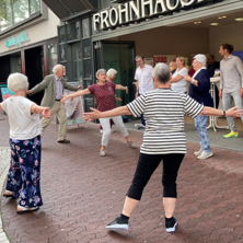Eine Gruppe älterer Menschen mach mitten in der Stadt Bewegungsübungen.