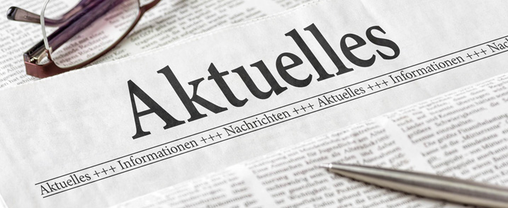 Ausschnitt einer Zeitung mit der Aufschrift: Aktuelles. Darauf liegen ein Kugelschreiber und eine Lesebrille.