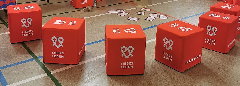 rote Würfel mit der Aufschrift "Liebesleben" liegen auf dem Boden einer Turnhalle