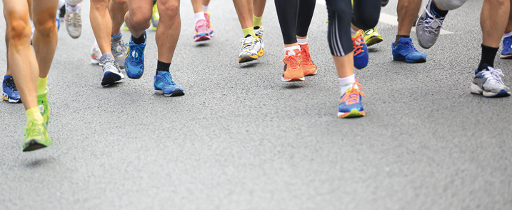 Ausschnittansicht von Füßen mehrerer Personen in Sportschuhen, die einen Laufsport betreiben.