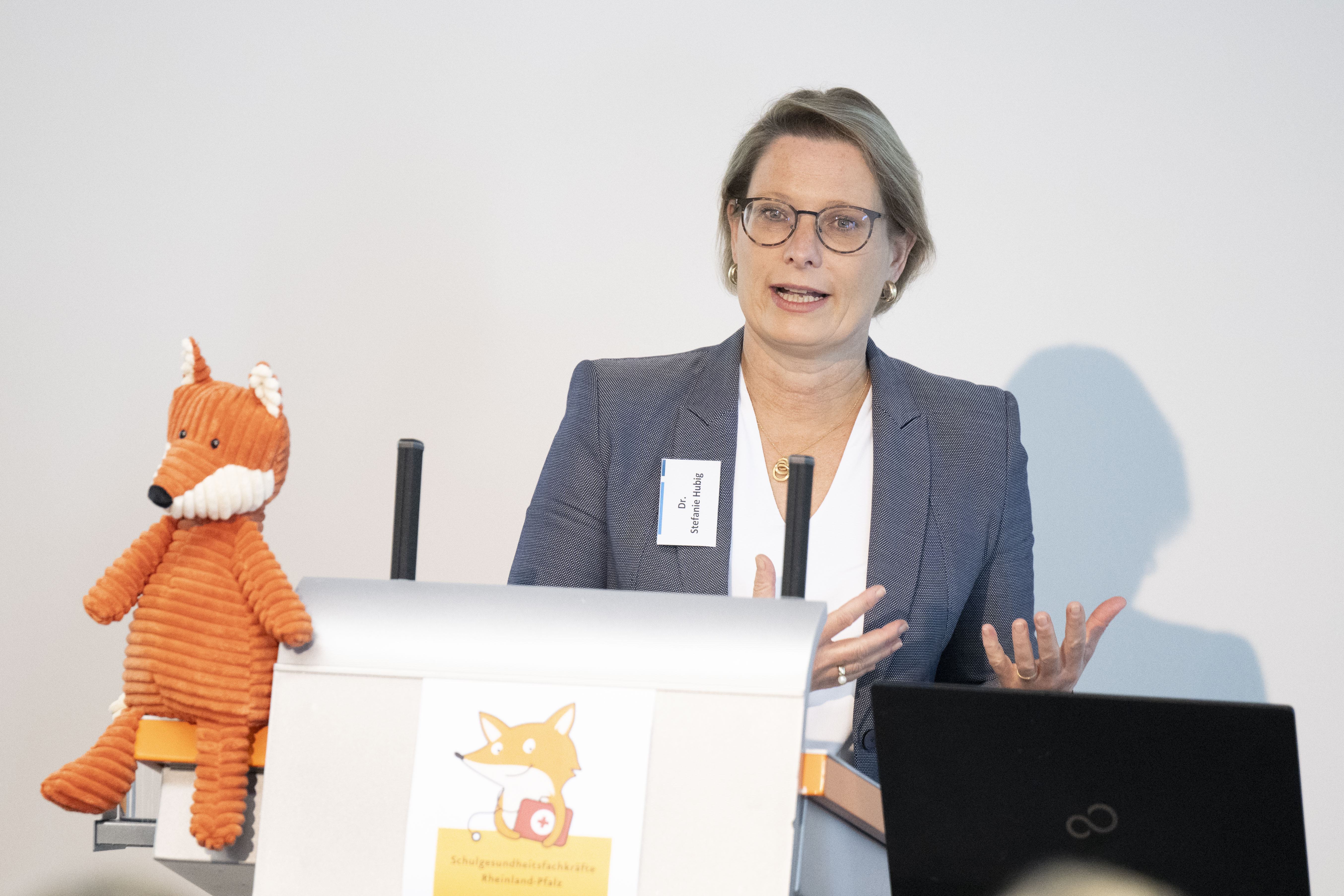 Bildungsministerin Dr. Stefanie Hubig als Rednerin vor zwei Bildschirmen und dem Maskottchen: ein Fuchs als Kuscheltier.